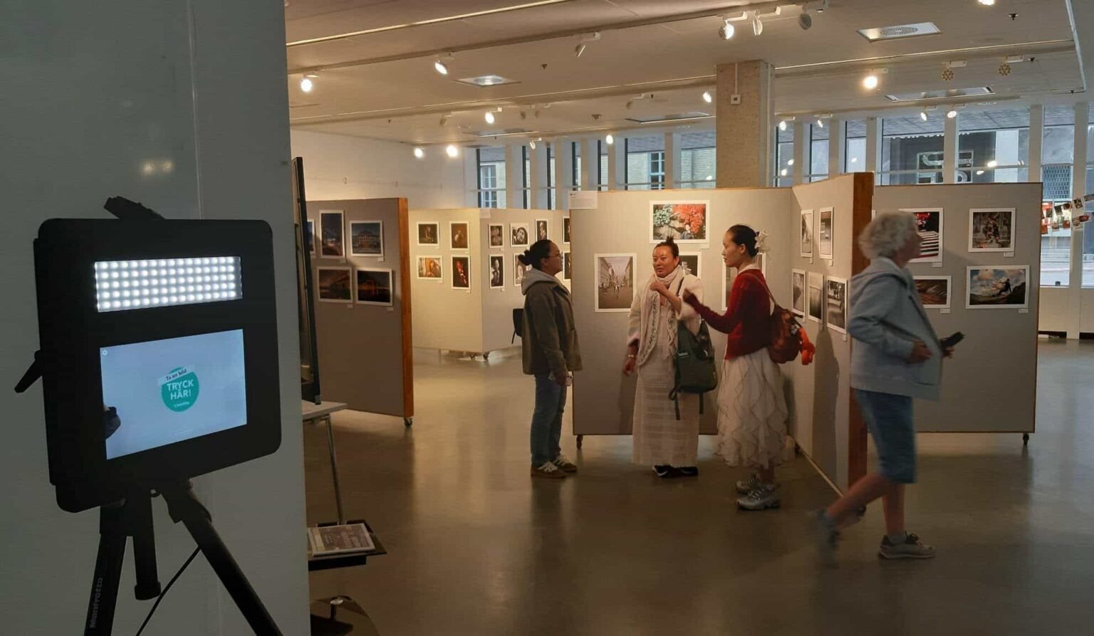 Visitors talking in a photography exhibition gallery with a photo booth setup in the foreground.